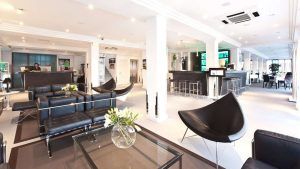 El elegante vestíbulo del hotel cuenta con asientos de cuero negro, mesas de cristal y un bar al fondo, reflejando el encanto de Escapada OD Ocean Drive con desayuno (Ibiza). Ideal para quienes desean una escapada a Ibiza. - ForTwo - Planes para parejas