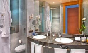 Transforme su baño en la elegancia moderna del Hotel SH Valencia Palace con lavabos dobles, encimeras de mármol, un espejo de pared, lujosas toallas y una acogedora bata. - ForTwo - Planes para parejas