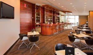 Un elegante y moderno bar en el Hotel SH Valencia Palace, con detalles en madera, mesas redondas y elegantes sillas negras. El acogedor espacio incluye una barra completamente equipada con cómodos taburetes, un reflejo perfecto del estilo del hotel. - ForTwo - Planes para parejas