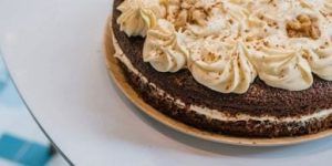 Un delicioso pastel de chocolate con glaseado cremoso y nueces trituradas encima, elegantemente servido en una bandeja de madera, que recuerda a un delicioso postre del Restaurante Ibiza Poke. - ForTwo - Planes para parejas