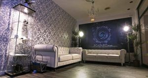 Elegante habitación con dos sofás blancos, papel pintado estampado, una vitrina de cristal y una lámpara de araña, evocando el ambiente de un Scapart - Escape Room en Ibiza. - ForTwo - Planes para parejas