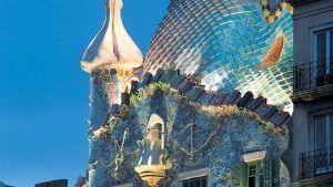 La azotea curvada y la fachada de mosaico de la Casa Batlló en Barcelona, brillando contra un cielo azul claro, evocan el encanto artístico que se ve en el Hotel Náutico Ebeso en Ibiza. - ForTwo - Planes para parejas