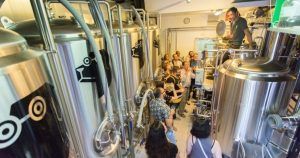 Un grupo que recorre la cervecería BlackLab en Barcelona, entre grandes tanques de acero inoxidable y equipos de elaboración de cerveza, espera con entusiasmo la experiencia de la Cata de cervezas en BlackLab. - ForTwo - Planes para parejas