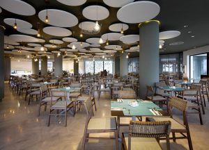 El interior de un moderno restaurante presenta paneles de techo circulares, sillas de madera y mesas con detalles en turquesa, que evocan el ambiente chic de Ibiza, como el del Hard Rock Hotel (Ibiza). - ForTwo - Planes para parejas
