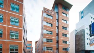Un edificio contemporáneo de varios pisos con paneles de color marrón anaranjado y grandes ventanales evoca el elegante encanto del Hotel Náutico Ebeso de Ibiza, con "Capri" en su fachada. - ForTwo - Planes para parejas