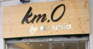 Un cartel en un escaparate muestra "Cata de vinos en Barcelona" de km.O sobre un fondo de madera encima de una entrada, invitando a los transeúntes a explorar los sabores de Barcelona. - ForTwo - Planes para parejas