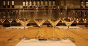 Copas de vino vacías sobre una mesa de madera crean el escenario perfecto para una "Cata de vinos en Barcelona", con estantes llenos de botellas que evocan el encanto de una bodega local. - ForTwo - Planes para parejas