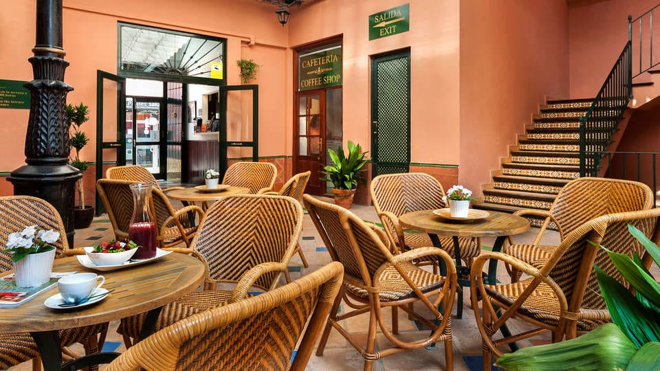 La "Escapada con desayuno y crucero en barco por el Guadalquivir (Sevilla)" ofrece un lugar ideal para desayunar con sillas de mimbre y macetas. Una escalera ofrece vistas a la actividad cercana y al río, con una salida despejada para un acceso cómodo. - ForTwo - Planes para parejas