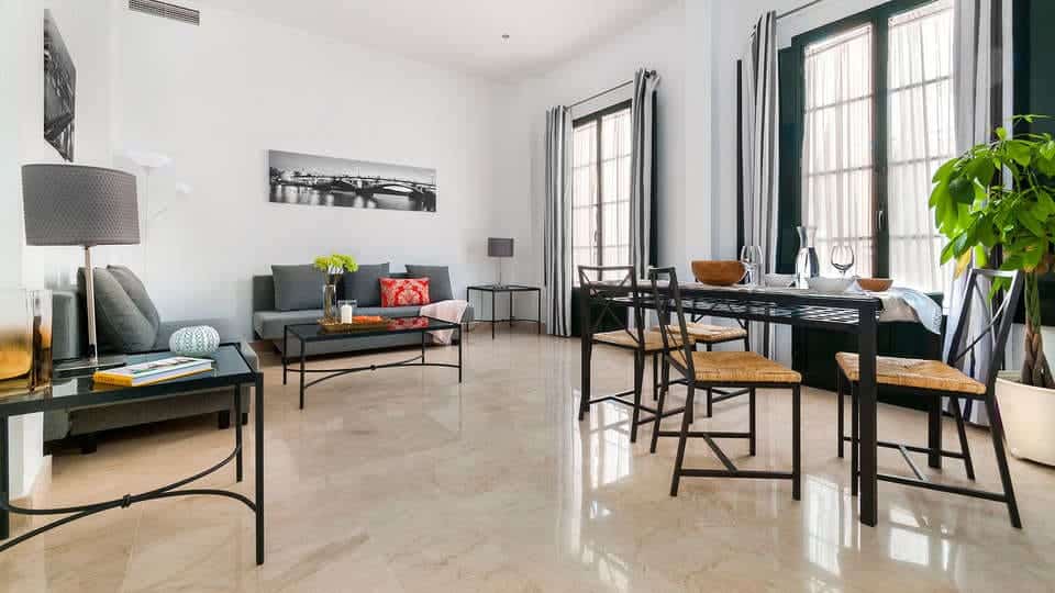Una luminosa sala de estar y comedor con una decoración moderna y vegetación da al resplandeciente Guadalquivir a través de grandes ventanales, realzados por cortinas transparentes, que complementan una "Escapada con desayuno y crucero en barco por el Guadalquivir (Sevilla). - ForTwo - Planes para parejas
