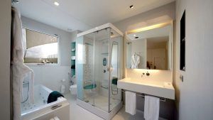 El moderno baño del Hotel Neptuno incluye una elegante ducha, bañera y lavabo. Las suaves toallas bajo un espejo de pared añaden lujo, evocando la elegancia de la Escapada en el Hotel Neptuno con desayuno y cava (Valencia). - ForTwo - Planes para parejas