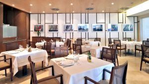 La Escapada en el Hotel Neptuno con desayuno y cava (Valencia) ofrece un acogedor interior de restaurante con manteles blancos, sillas de madera y arte mural náutico, perfecto para un relajante desayuno con cava. - ForTwo - Planes para parejas