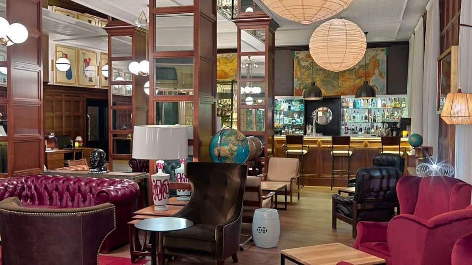 Acogedor bar con asientos de cuero rojo, decoración en forma de globo terráqueo, paneles de madera e iluminación ambiental, ideal para una experiencia Escapada en el hotel H10 Montcada con extras (Barcelona). - ForTwo - Planes para parejas