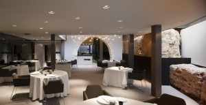 El Hotel Caro de Valencia cuenta con un elegante restaurante con mesas redondas cubiertas con manteles blancos bajo un encantador arco de piedra. - ForTwo - Planes para parejas