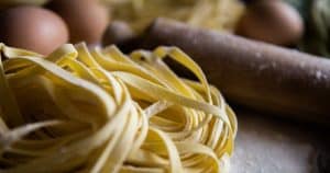 Primer plano de nidos de pasta fresca sobre una superficie enharinada con huevos y un rodillo, que recuerdan la deliciosa experiencia "Curso de pasta fresca en Madrid con degustación. - ForTwo - Planes para parejas