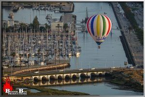 Un colorido globo aerostático sobrevolaba el puerto deportivo, con barcos abajo, mientras los vehículos cruzaban un puente cercano. Esta encantadora escena encarnaba la esencia de un "Vuelo estándar en globo por Cataluña con Globus (Barcelona)", que evocaba una mañana soleada en la vibrante Barcelona. - ForTwo - Planes para parejas