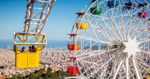 En una cabina amarilla de la colorida noria del Parque de Atracciones del Tibidabo, los visitantes disfrutan de impresionantes vistas del paisaje urbano y el océano. Las entradas para el parque de atracciones del Tibidabo (Barcelona) ofrecen acceso a esta icónica atracción y experiencias inolvidables. - ForTwo - Planes para parejas