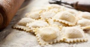 Raviolis enharinados sobre una superficie de madera junto a un rodillo capturan la esencia de la pasta fresca. Imagine esta escena en una cocina madrileña durante el "Curso de pasta fresca en Madrid con degustación". - ForTwo - Planes para parejas