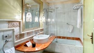 Elegante baño con superficies de mármol, lavabo redondo y bañera, ideal para una escapada con desayuno y botella de cava a una casa del siglo XVIII en Sevilla. Lámparas decorativas cuelgan con elegancia sobre el espejo. - ForTwo - Planes para parejas