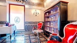 Disfrute de una elegante habitación con sillas rojas, azulejos ornamentados, una mesa auxiliar con aires de una casa del S. XVIII, frascos decorativos en una estantería y la cálida luz de la lámpara de araña. Perfecto para una "Escapada con desayuno y botella de cava a una casa del S. XVIII (Sevilla)" para empezar el día. - ForTwo - Planes para parejas