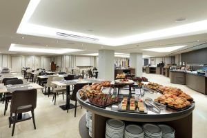 El amplio comedor del Hotel Eurostars Rey Don Jaime (Valencia) cuenta con mesas y sillas alrededor de un buffet repleto de pasteles y postres variados. - ForTwo - Planes para parejas