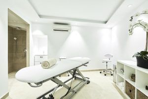 La minimalista sala de spa del Hotel Eurostars Ibiza incluye una camilla de masajes, una toalla enrollada, una orquídea y una zona de ducha, todo ello en un ambiente sereno y luminoso. - ForTwo - Planes para parejas