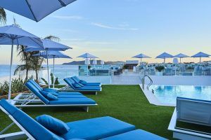 Disfrute de la piscina en la azotea del Hotel Eurostars Ibiza, con tumbonas y sombrillas azules y espectaculares vistas al mar bajo un cielo soleado. Relájese en el lujo de este oasis hotelero en el corazón de Ibiza. - ForTwo - Planes para parejas