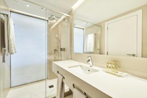 El moderno baño del Hotel Eurostars Ibiza cuenta con una elegante ducha de cristal, un gran espejo y un impecable lavabo blanco. La suave iluminación realza el espacio con toallas y artículos de aseo cuidadosamente ordenados para su comodidad. - ForTwo - Planes para parejas