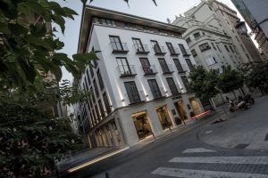 Vista de la calle del moderno Hotel Vincci Mercat (Valencia) en color blanco, con pequeños balcones y rodeado de árboles, enclavado entre encantadores edificios antiguos. - ForTwo - Planes para parejas
