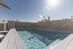 El Hotel Vincci Mercat de Valencia cuenta con una piscina en la azotea con agua cristalina y una resistente barandilla de metal, que ofrece el oasis urbano perfecto con vistas al vibrante horizonte de la ciudad bajo un cielo iluminado por el sol. - ForTwo - Planes para parejas