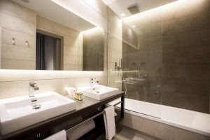 Un baño elegante inspirado en el Hotel Vincci Mercat (Valencia), que cuenta con un lavabo doble, grifería de pared y una bañera con mampara de cristal. - ForTwo - Planes para parejas
