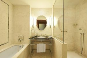 Disfrute de un elegante baño con decoración de mármol, espejo ovalado y grifería de lujo en el Hotel The Westin (Valencia). Disfrute de una lujosa bañera y una ducha con mampara de cristal en este exquisito oasis hotelero. - ForTwo - Planes para parejas