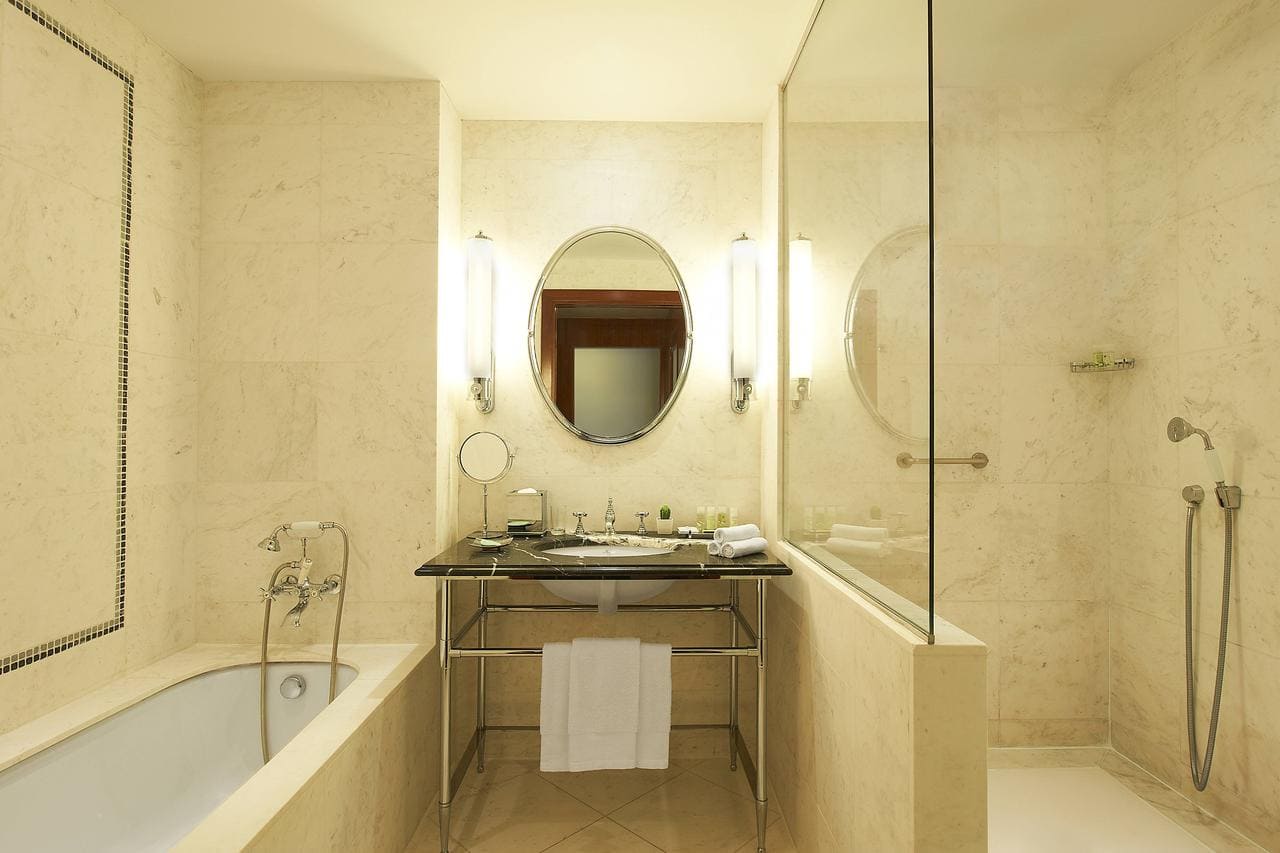 Disfrute de un elegante baño con decoración de mármol, espejo ovalado y grifería de lujo en el Hotel The Westin (Valencia). Disfrute de una lujosa bañera y una ducha con mampara de cristal en este exquisito oasis hotelero. - ForTwo - Planes para parejas