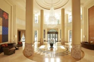 El vestíbulo del Hotel The Westin en Valencia cuenta con suelos de mármol, una gran lámpara de araña, imponentes columnas y una elegante zona de estar circular. - ForTwo - Planes para parejas