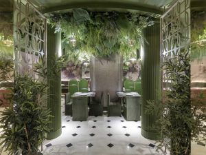 Experimente la esencia de Madrid en el Restaurante Purnima, donde el Menú degustación de cocina india realza un área de comedor con decoración verde, follaje en el techo, asientos elegantes y un ambiente vibrante flanqueado por columnas y plantas. - ForTwo - Planes para parejas