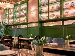 Experimente el delicioso menú indio del Restaurante Purnima en Madrid, que cuenta con un ambiente acogedor con paredes verdes, mesas de mármol, plantas en macetas y estantes que exhiben frascos y platos. - ForTwo - Planes para parejas