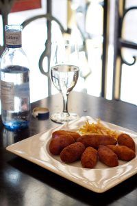 Un plato de croquetas con patatas fritas reposa en la mesa junto a una botella de agua y un vaso. Este delicioso plato forma parte de la Oferta: cena para dos en Bodegas Mezquita, menú especial Mezquita (Córdoba), que captura la esencia y la tradición culinaria de Bodegas Mezquita. - ForTwo - Planes para parejas