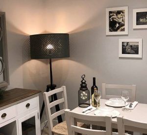 Acogedor comedor con mesa para dos con la Oferta de Bodegas Mezquita: cena para dos en Bodegas Mezquita, menú especial Mezquita (Córdoba) y lámpara de pie iluminada; Las fotografías en blanco y negro colgadas en las paredes capturan el encanto de Córdoba. - ForTwo - Planes para parejas