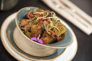 Disfrute de un plato de verduras asadas con brotes y flores comestibles, que recuerda a la Oferta degustación Sabores de India del restaurante Bangalore en Madrid, bellamente servida en platos apilados. - ForTwo - Planes para parejas