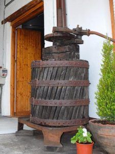 El antiguo lagar de la bodega Muñoz Martín se alza elegantemente junto a la puerta, evocando el encanto de una bodega, mientras que una pequeña planta en maceta añade un toque de verde al ambiente rústico. - ForTwo - Planes para parejas