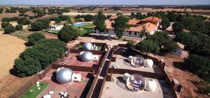 Una vista aérea muestra el encantador paisaje de una zona rural, con tiendas de burbujas transparentes del Hotel Zielo Las Beatas ubicadas cerca de una encantadora casa, rodeadas de frondosos árboles y extensos campos. - ForTwo - Planes para parejas