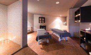 El Circuito Spa para 2 personas en Adeje ofrece un oasis de tranquilidad con iluminación tenue, dos mesas de masaje y estantes llenos de velas y toallas. - ForTwo - Planes para parejas