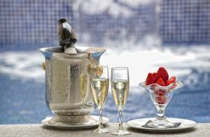 Champán enfriándose en una cubitera con hielo, dos copas llenas y un bol de fresas junto a la piscina en el romántico Hotel íntimo para parejas: Zouk hotel en Madrid. - ForTwo - Planes para parejas