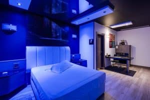 Este elegante refugio en Madrid, el Hotel Zouk, ofrece una habitación moderna con iluminación azul, cama blanca, escritorio y suelo de madera. Las paredes decoradas con obras de arte y un diseño minimalista crean un ambiente sereno, ideal para parejas. - ForTwo - Planes para parejas
