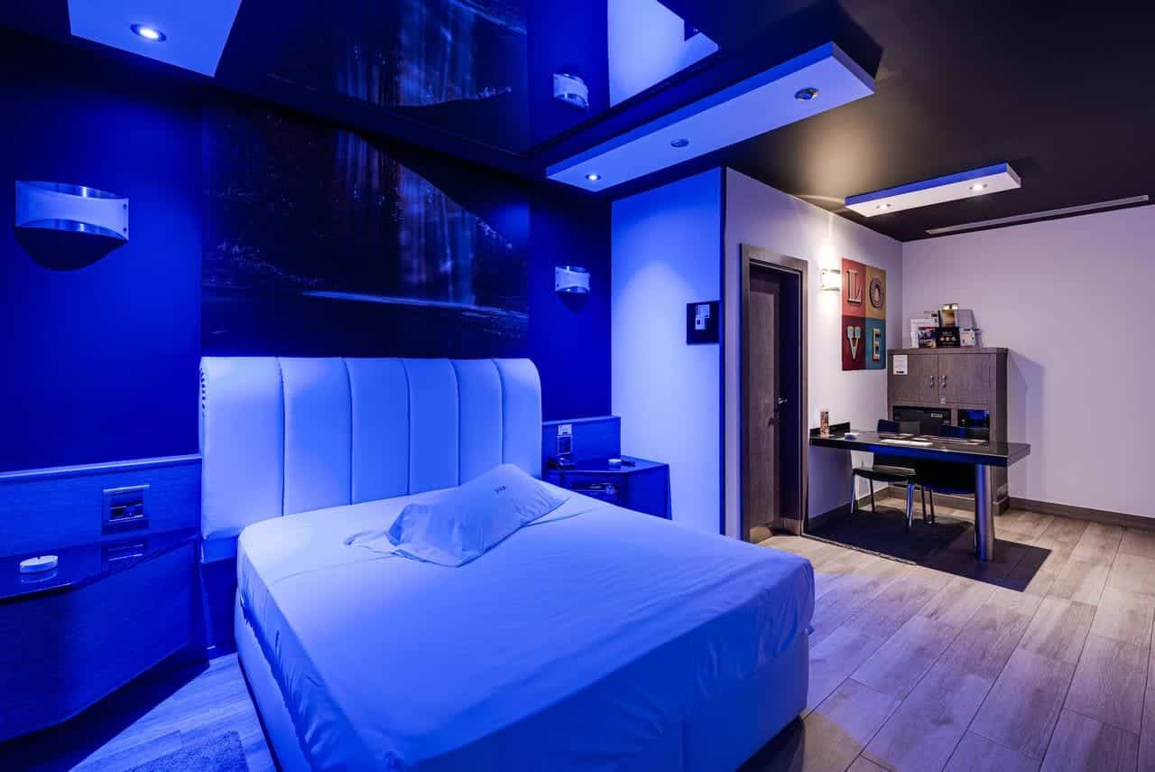 Este elegante refugio en Madrid, el Hotel Zouk, ofrece una habitación moderna con iluminación azul, cama blanca, escritorio y suelo de madera. Las paredes decoradas con obras de arte y un diseño minimalista crean un ambiente sereno, ideal para parejas. - ForTwo - Planes para parejas