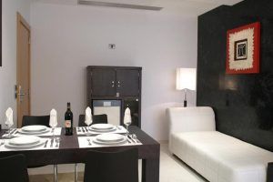 Un moderno comedor diseñado para parejas incluye una mesa negra, sillas blancas, un diván blanco y arte de pared minimalista, que refleja el ambiente íntimo del Hotel íntimo para parejas: Zouk hotel en Madrid. - ForTwo - Planes para parejas