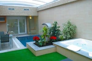 Disfrute de un romántico retiro en nuestra acogedora piscina cubierta, que evoca el ambiente del hotel Zouk de Madrid. Rodeada de exuberante vegetación, cuenta con un jacuzzi bajo techo de cristal y elegantes muebles de exterior, ideal para parejas que buscan lujo y tranquilidad. - ForTwo - Planes para parejas