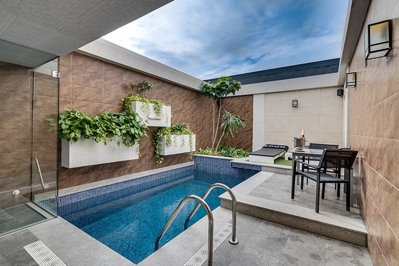 La íntima zona de piscina al aire libre del Zouk Hotel (Madrid) cuenta con exuberantes plantas, tumbonas y una mesa dispuesta bajo un cielo nublado, perfecta para escapadas en pareja. - ForTwo - Planes para parejas
