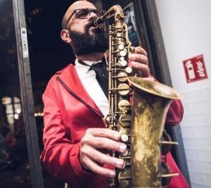 Un hombre con una chaqueta roja toca el saxofón en el interior, ofreciendo música en vivo en vivo en Martes de música en vivo y pizza en el Restaurante Leccabaffi (Barcelona). - ForTwo - Planes para parejas