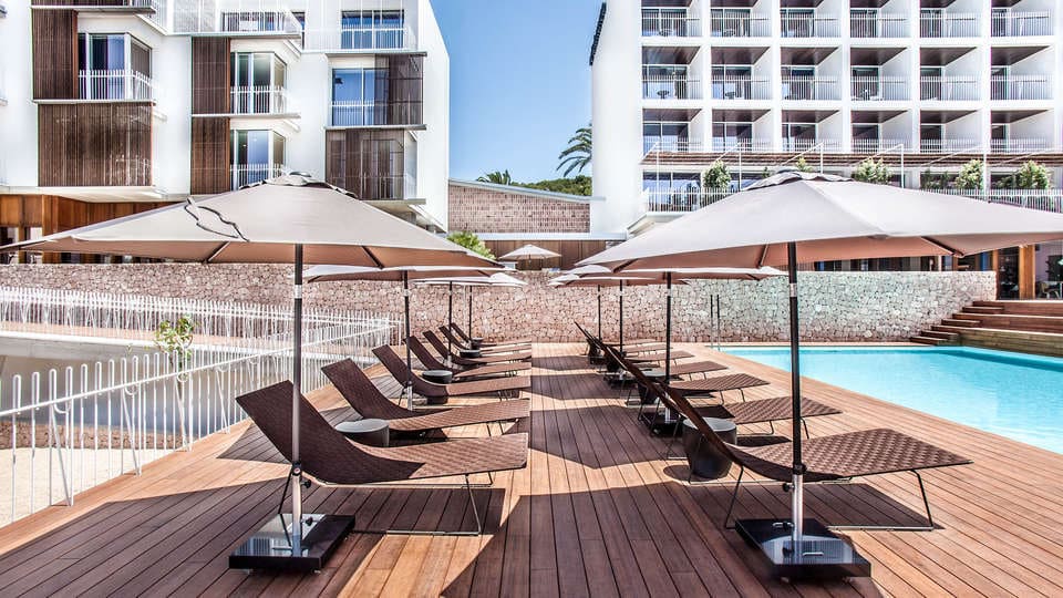 Tumbonas y sombrillas en una terraza rodeada de modernos edificios blancos evocan la serenidad y el lujo de Barcelona. Este entorno apacible complementa a la perfección el encanto innovador de Experiencia Kaitai en Tunateca Balfegó, ideal para disfrutar de la relajación y el estilo. - ForTwo - Planes para parejas