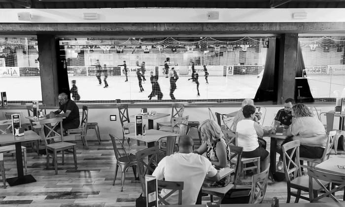 La gente en un acogedor restaurante, con estilo de iglú, disfruta de patinaje sobre hielo para dos en Igloo (Granada) mientras ven un emocionante partido de hockey sobre hielo a través de una gran ventana. - ForTwo - Planes para parejas